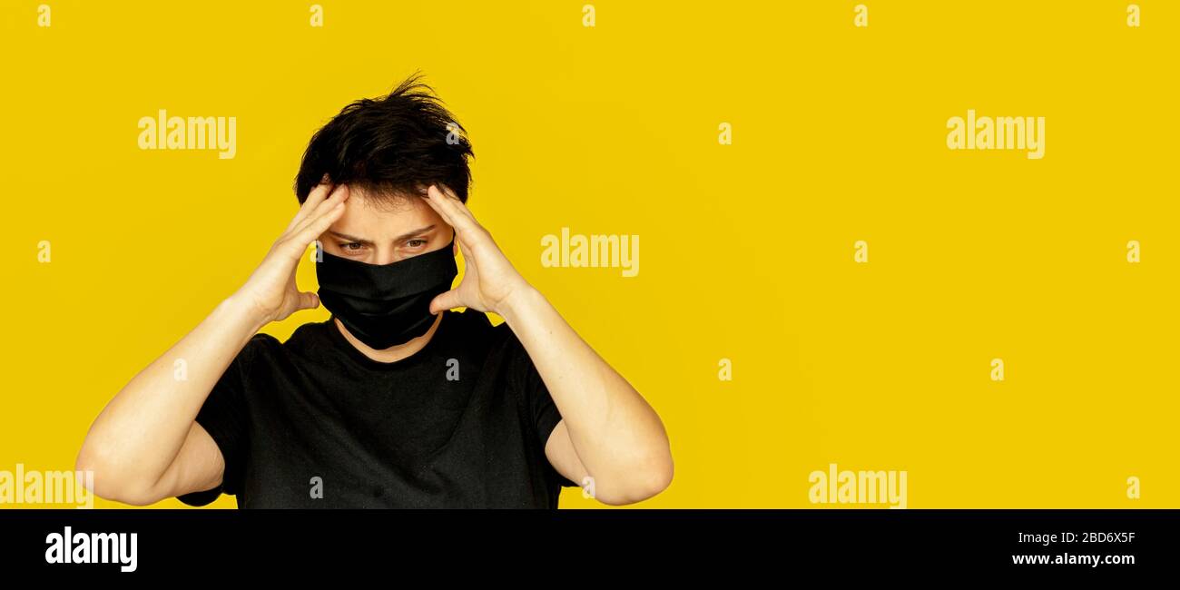 Mädchen Brünette kurze Haare schwarz medizinische Maske hält ihren Kopf Mit ihren Händen Emotion nervös Banner gelben Hintergrund Stockfoto