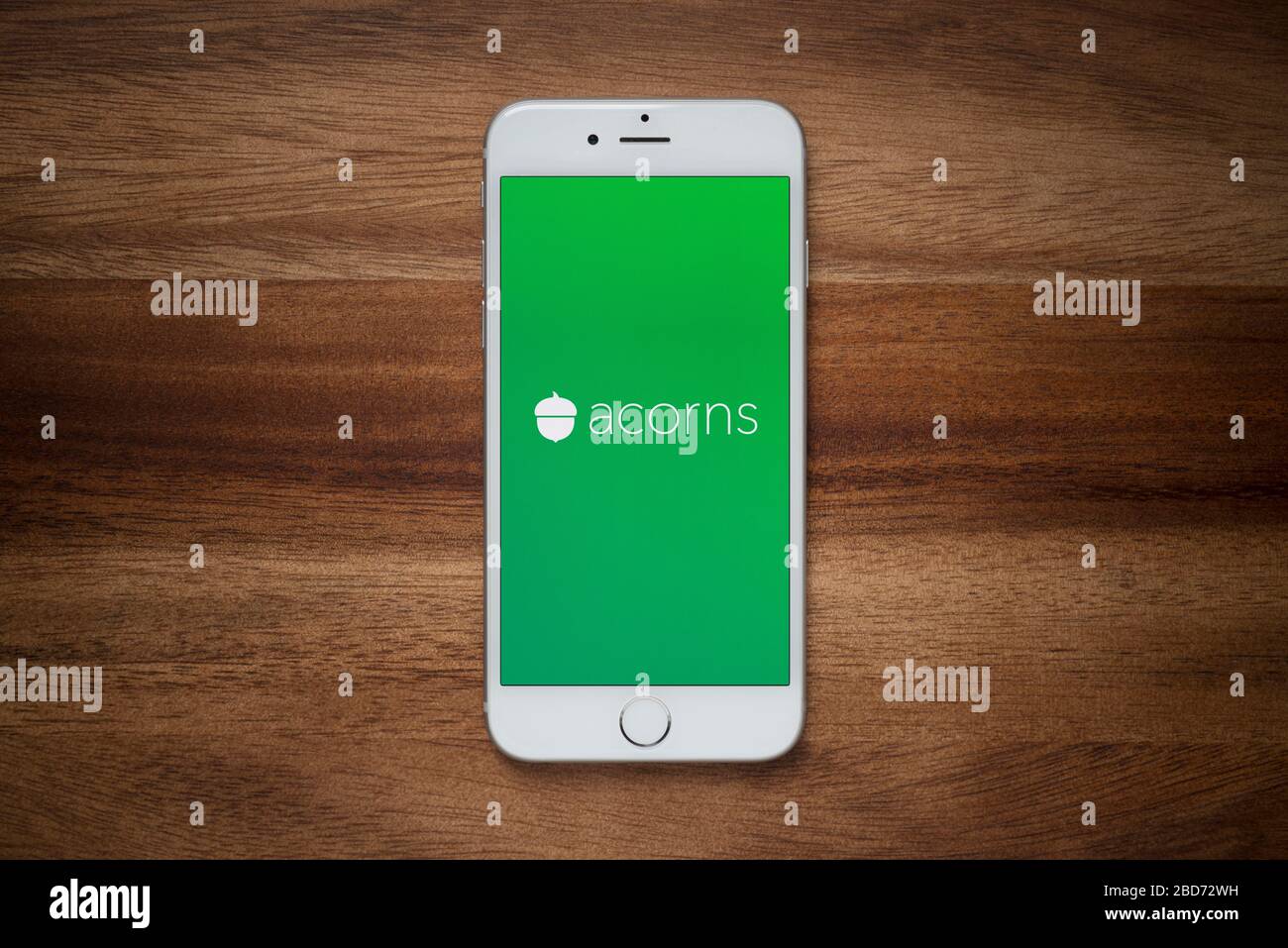 Ein iPhone mit dem Logo der Firma Acorns ruht auf einem einfachen Holztisch (nur für redaktionelle Zwecke). Stockfoto