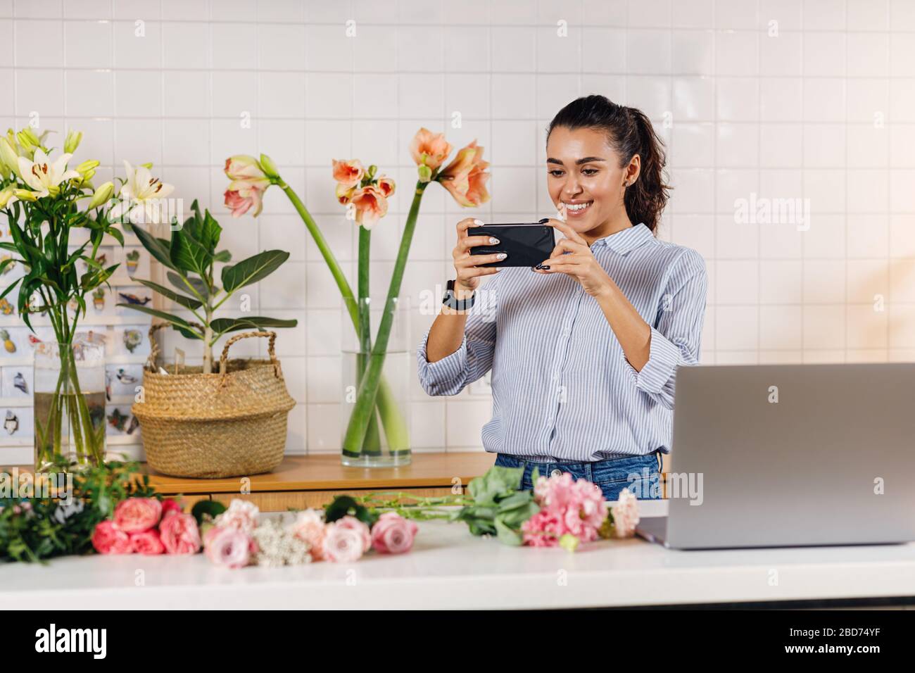 Lächelnde Frau, die Fotos auf einem Smartphone macht. Flower Shop-Besitzer, die Inhalte für ihren Online-Shop erstellen. Stockfoto