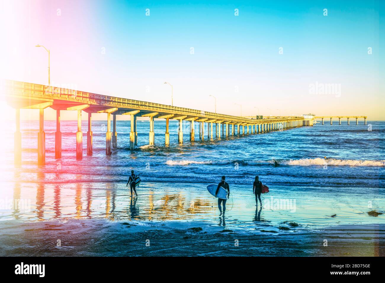 Surfergruppe am Ocean Beach mit dem Ocean Beach Pier. San Diego, CA, USA. Das Foto wurde mit einer Methode für leichte Lecks verarbeitet, um einen Vintage-Effekt zu erzielen. Stockfoto