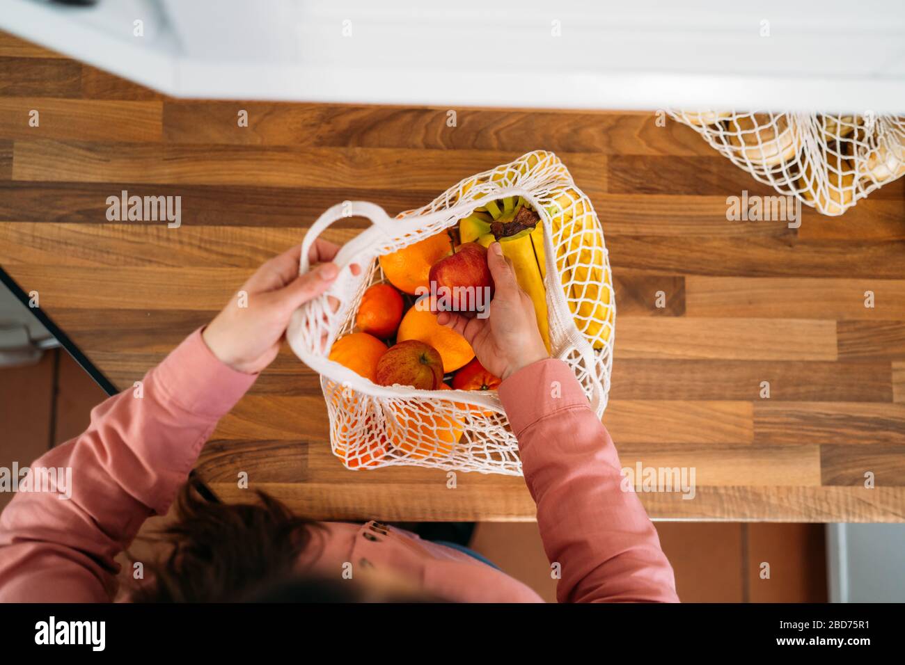 Draufsicht einer Frau, die Obst und Gemüse mit einer wiederverwendbaren Tasche aus biologischer Baumwolle und Netztaschen zum Einkaufen herausnimmt. Kein Abfall, Kunststofffreies Konzept. Stockfoto