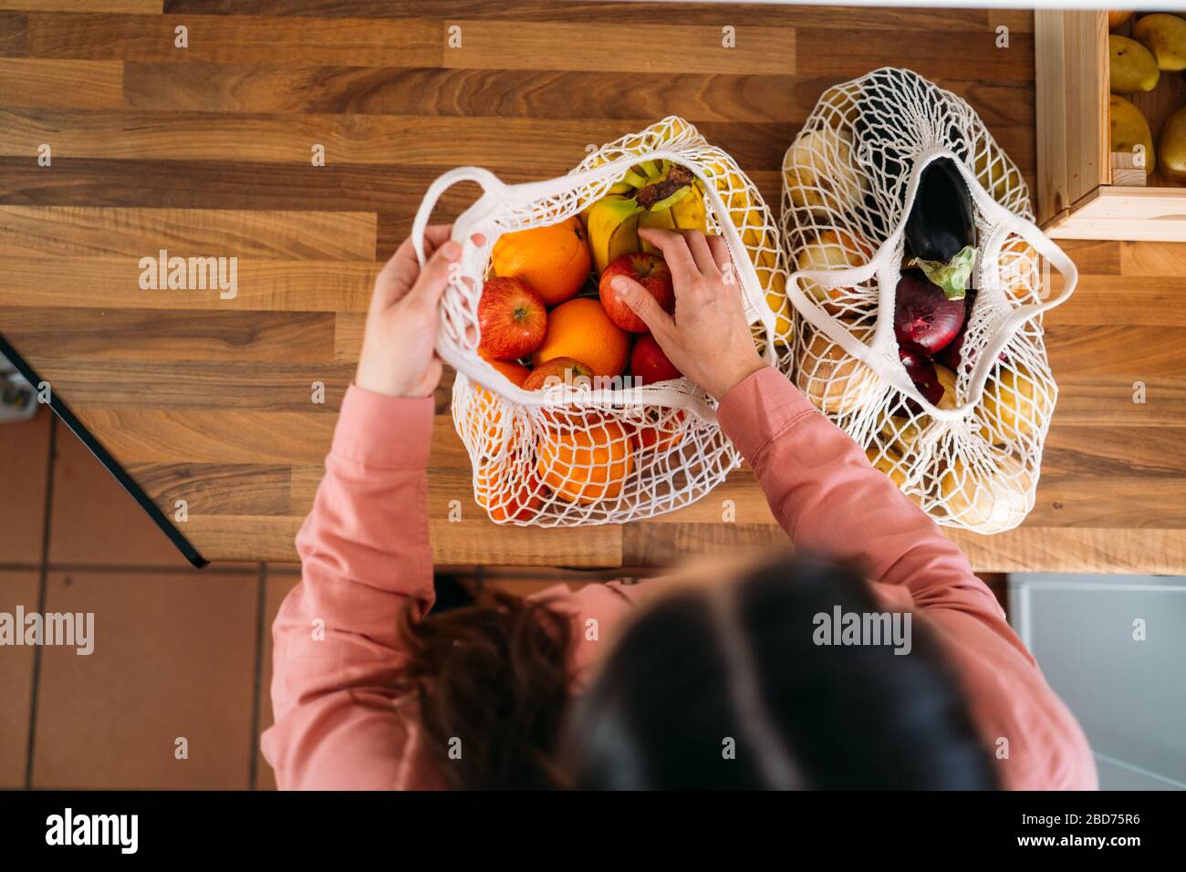 Draufsicht einer Frau, die Obst und Gemüse mit einer wiederverwendbaren Tasche aus biologischer Baumwolle und Netztaschen zum Einkaufen herausnimmt. Kein Abfall, Kunststofffreies Konzept. Stockfoto