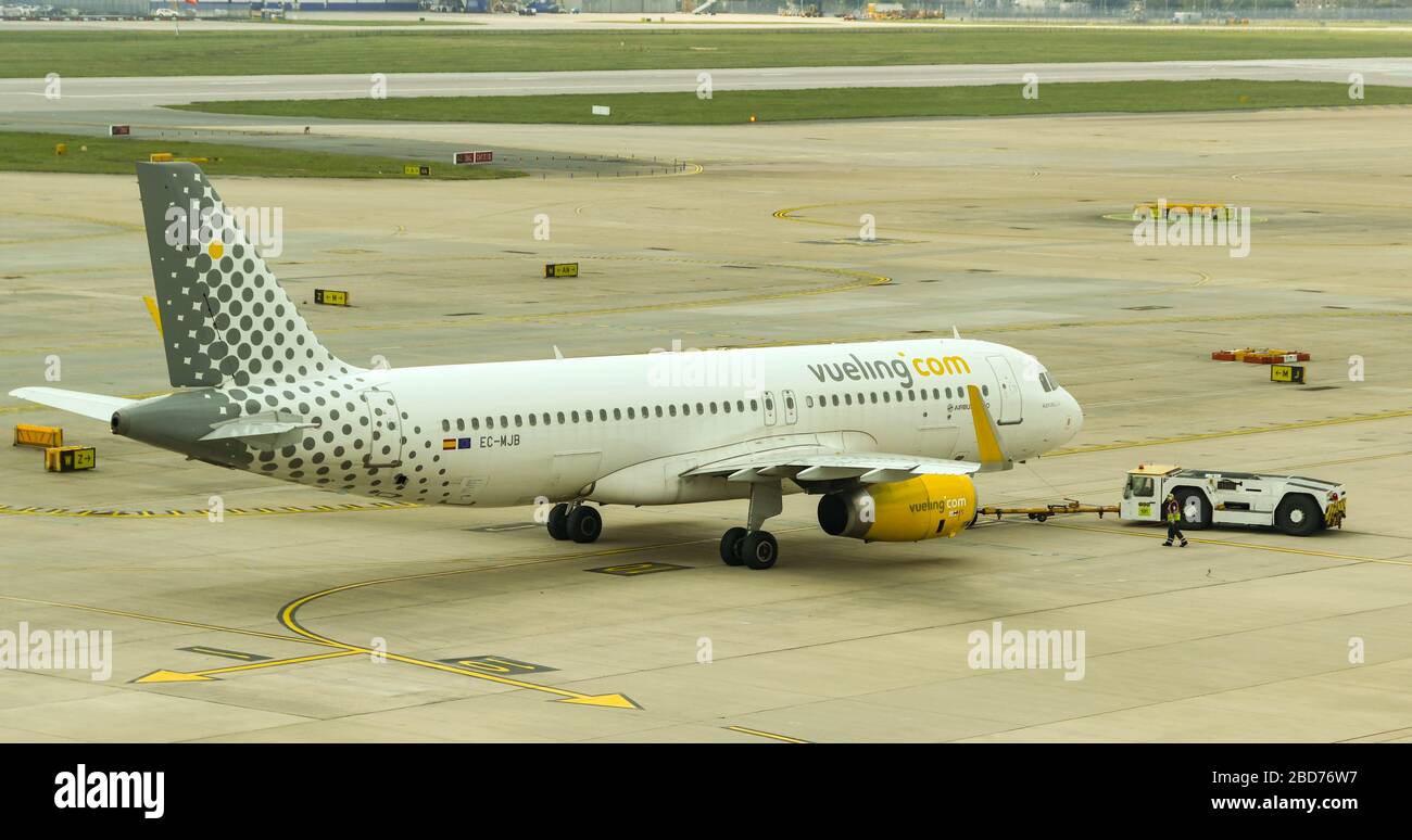 FLUGHAFEN LONDON-GATWICK - APRIL 2019: Airbus A320, der von der spanischen Fluggesellschaft Vueling betrieben wird, wird bei der Abfahrt von London Gatwick A von einem Schlepper zurückgedrängt Stockfoto