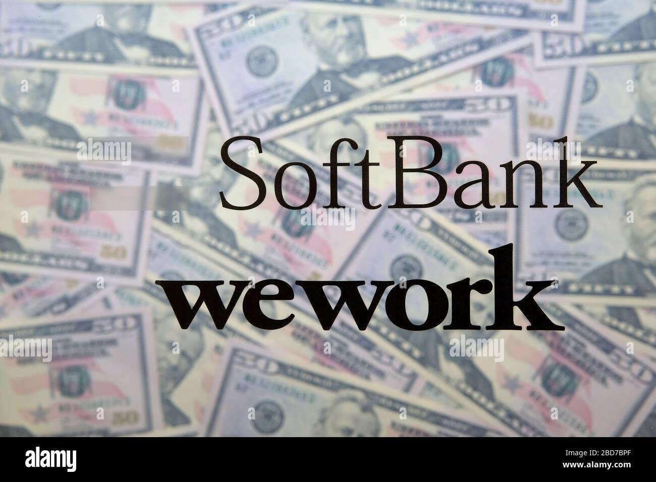 Softbank- und WeWork-Logos sind auf transparentem Folienfilm aufgedruckt und auf Dollar-Banknoten platziert.kein montageechtes Foto. Stockfoto