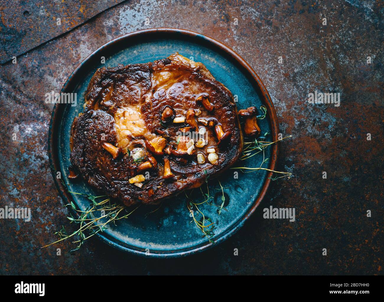 Saftiges Ribeye Steak vom Grill mit Pilzen, Zwiebeln und Thymian auf einem Teller, amerikanische Küche Stockfoto