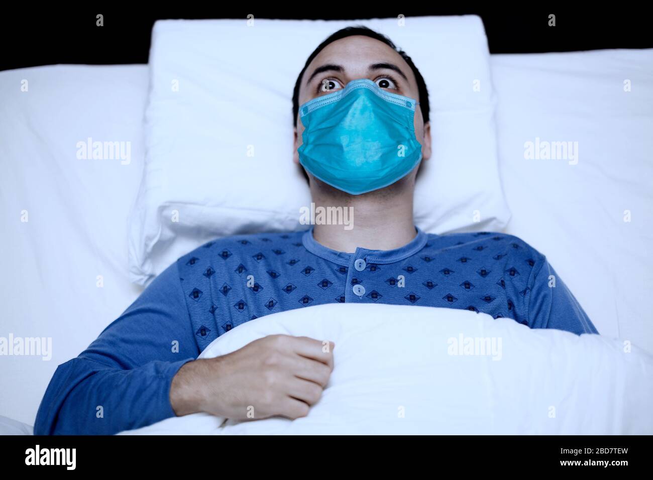 Porträt eines unomnic Mannes, der versucht, in seinem Bett zu schlafen, während er eine Maske trägt, Coronavirus Quarantänekonzept Stockfoto