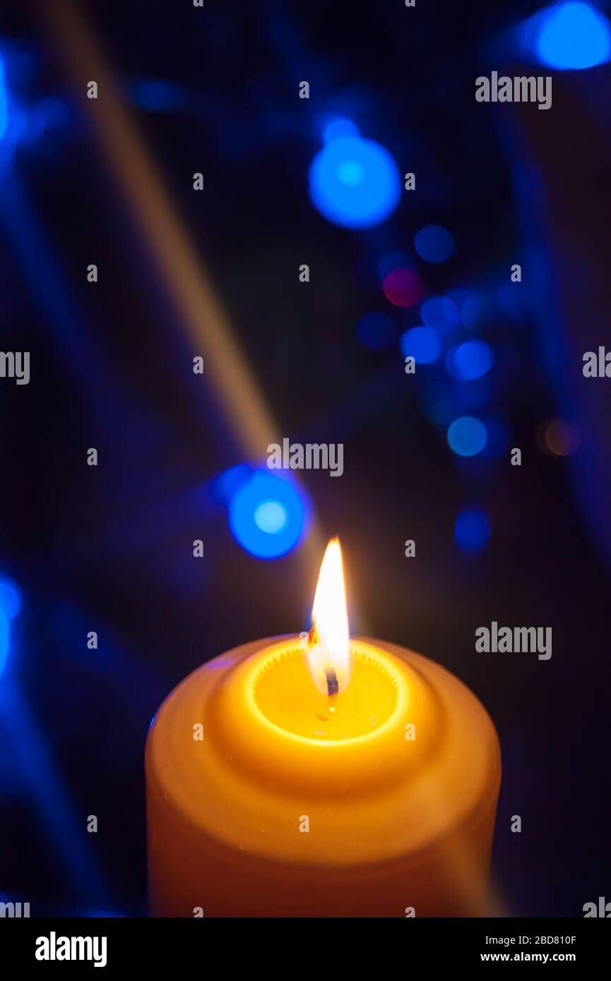 Eine große Kerze brennt vor dem Hintergrund einer Girlande mit strahlendem Licht. Vertikales Foto, Unschärfe. Mystische esoterische Romantik Divination Stimmung getauft Weihnachts-Karol-Setcer Stockfoto
