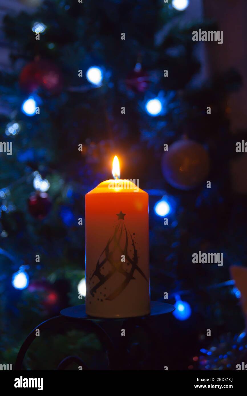 Eine große Kerze brennt vor dem Hintergrund einer Girlande mit strahlendem Licht. Vertikales Foto, Unschärfe. Mystische esoterische Romantik Divination Stimmung getauft Weihnachts-Karol-Setcer Stockfoto