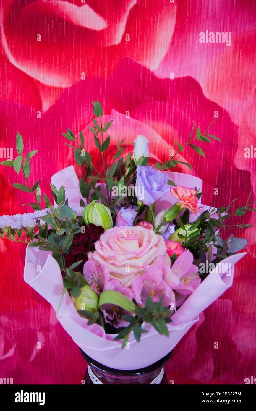 Ein zartes Blumenstrauß mit verschiedenen Blumen in einem hellrosa Wrapper steht in einer häuslichen Umgebung gegen eine bunte rosafarbene Wand. Vertikales Foto. Stockfoto