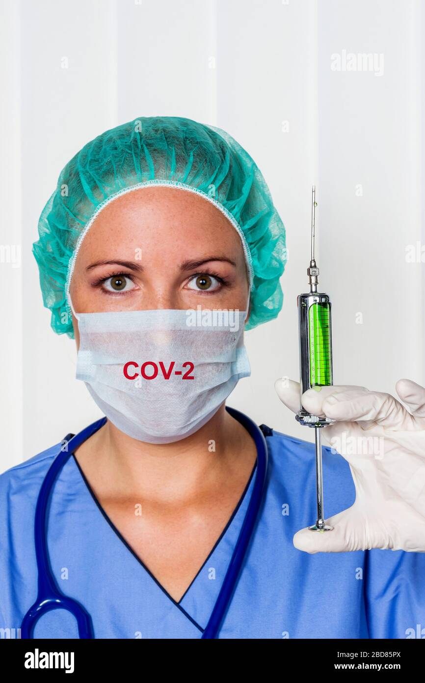 Weiblicher Chirurgiearzt in Srubs mit Spritze, Corona-Virus Stockfoto