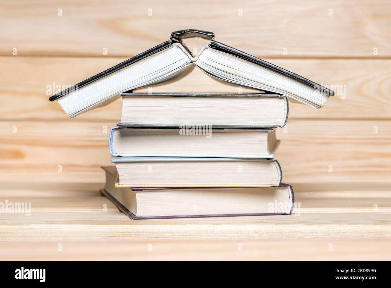 Das Konzept "zu Hause bleiben". Haus aus Büchern, die auf Holzgrund gehüpft sind. Stapel von Büchern. Bildungskonzept. Stapel von Büchern in Form eines Gebäudes. Buchen Stockfoto