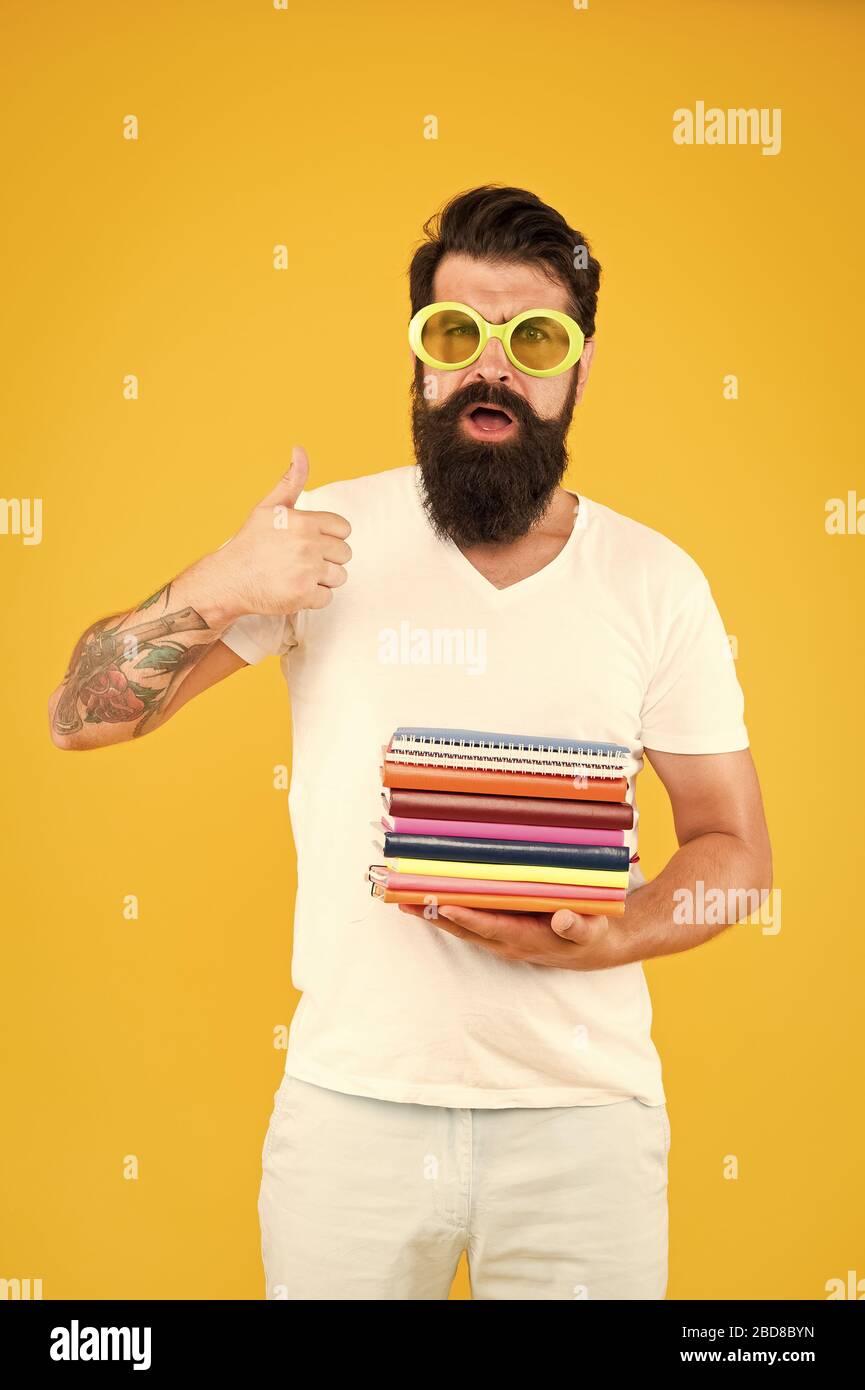 Ich lese gerne Bücher. Bärtiger Mann mit Büchern zeigt Daumen nach oben. Schule und Bildung. Privatunterricht. Starten. Bücher aus der Bibliothek ausleihen. Brauchen Sie mehr Bücher. Stockfoto