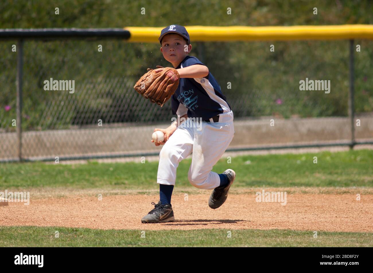 Little League-Feldspieler im Begriff, den Ball auf die erste Basis zu werfen Stockfoto