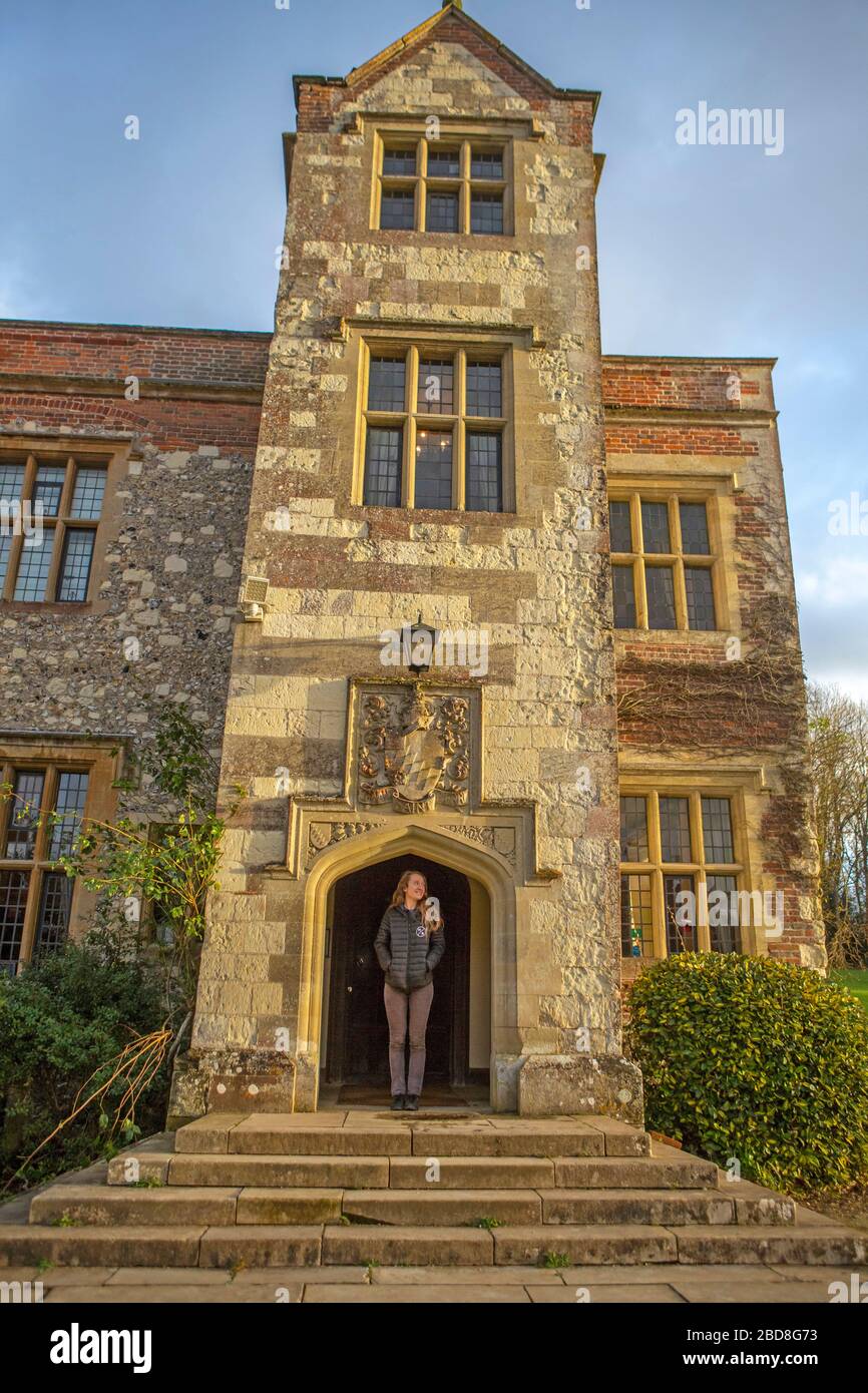 Junge Besucherin, die im Torbogen des Chawton House steht, mit der kunstvollen Steinschnitzerei direkt darüber Stockfoto