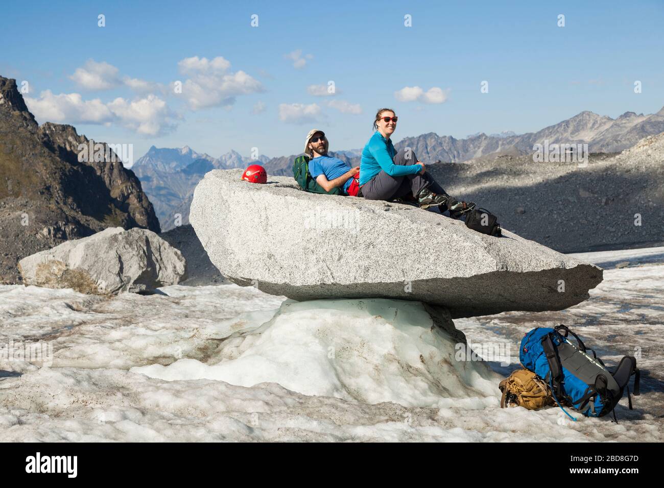 Ein Paar sitzt auf einem großen Gletschertafel (ein Felsen, der von einer von Schmelze beschatteten Eissäule gestützt wird) auf dem Snowbird-Gletscher, den Talkeetna Mountains, Alaska. Snowbi Stockfoto