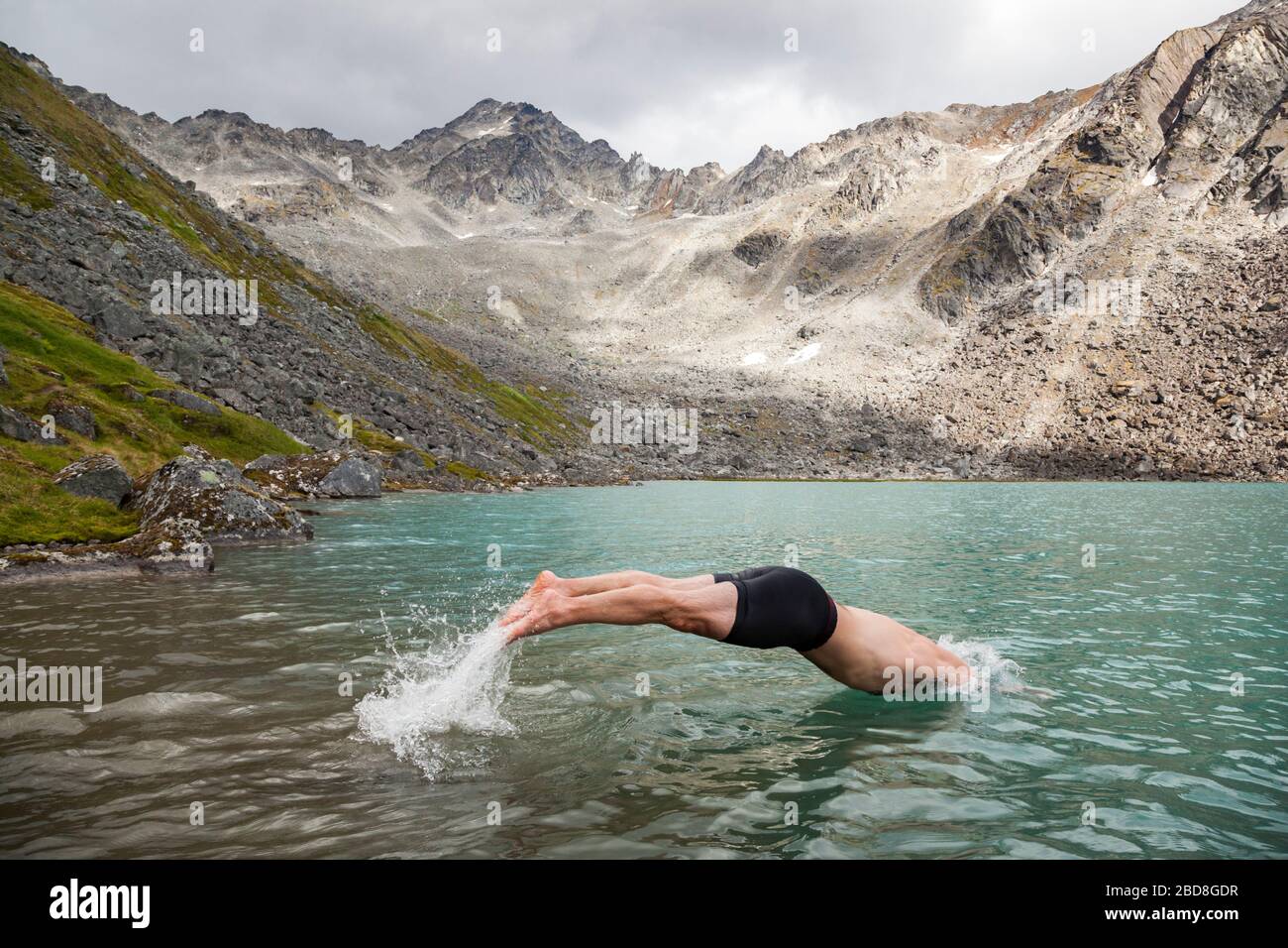 Ein Mann taucht zum Schwimmen in den Upper Reed Lake, Talkeetna Mountains, Alaska. Stockfoto