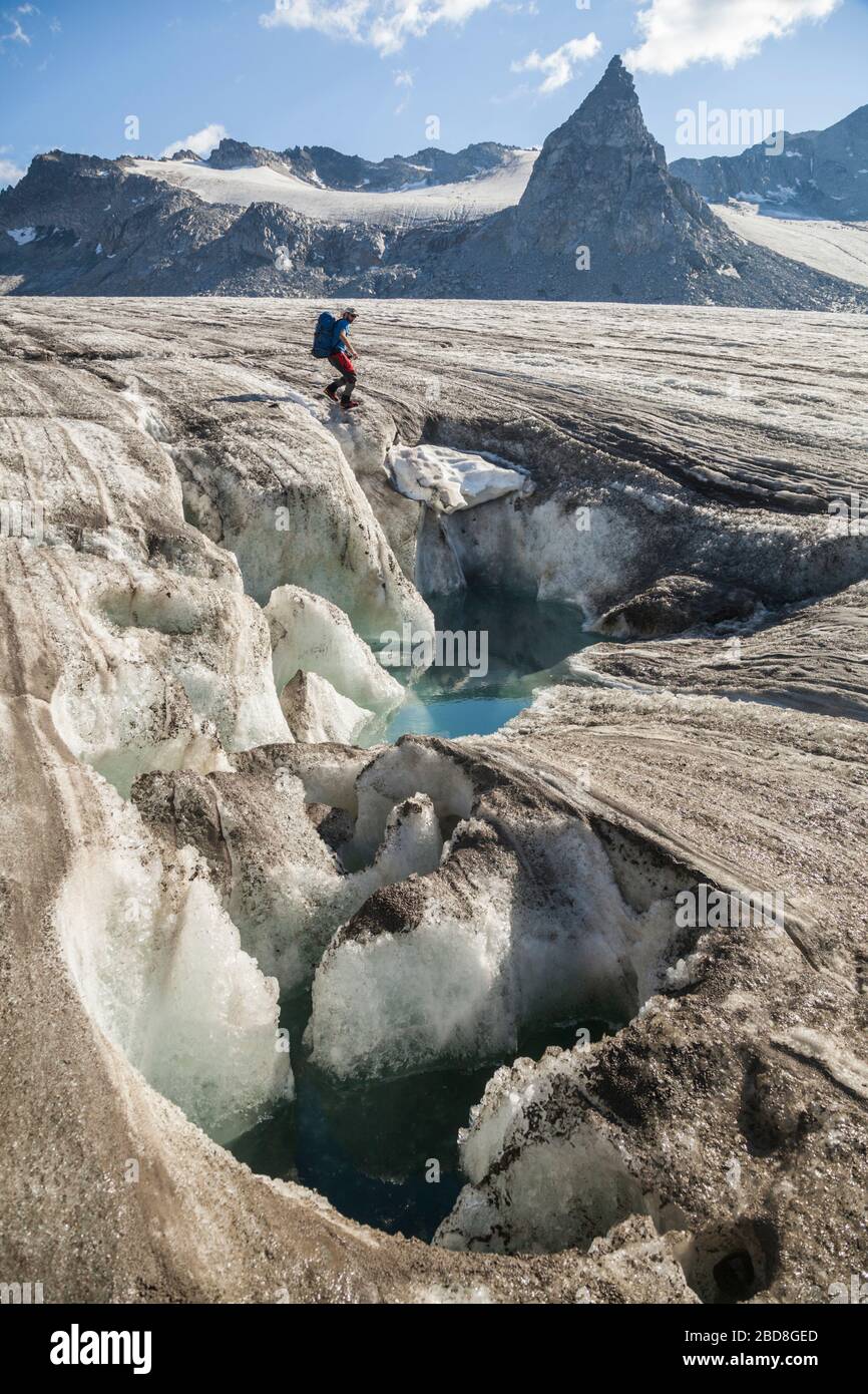 Ein Mann wandert an einem Schmelzwasserteich am Snowbird-Gletscher, den Talkeetna Mountains, Alaska vorbei. Ein Nunatak (auf einigen Karten Nunataq genannt) steht im Hintergrund. Stockfoto