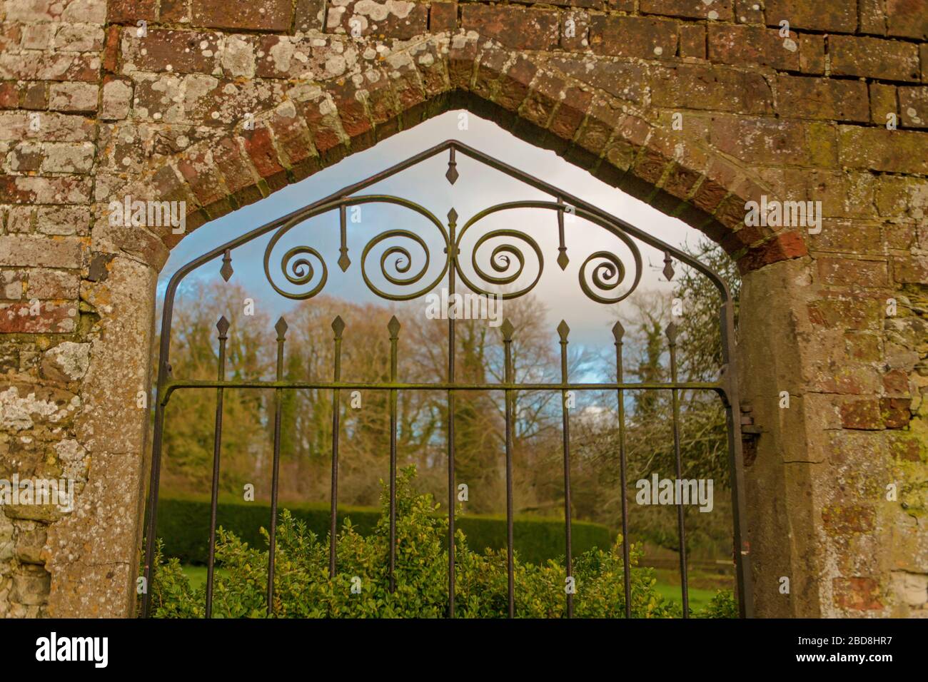 Schmiedeeiserne Tor Eingang zum ummauerten Garten mit Wald im Hintergrund bei Chawton House Garten zeigt Ziegel und Stein in der Wandkonstruktion Stockfoto