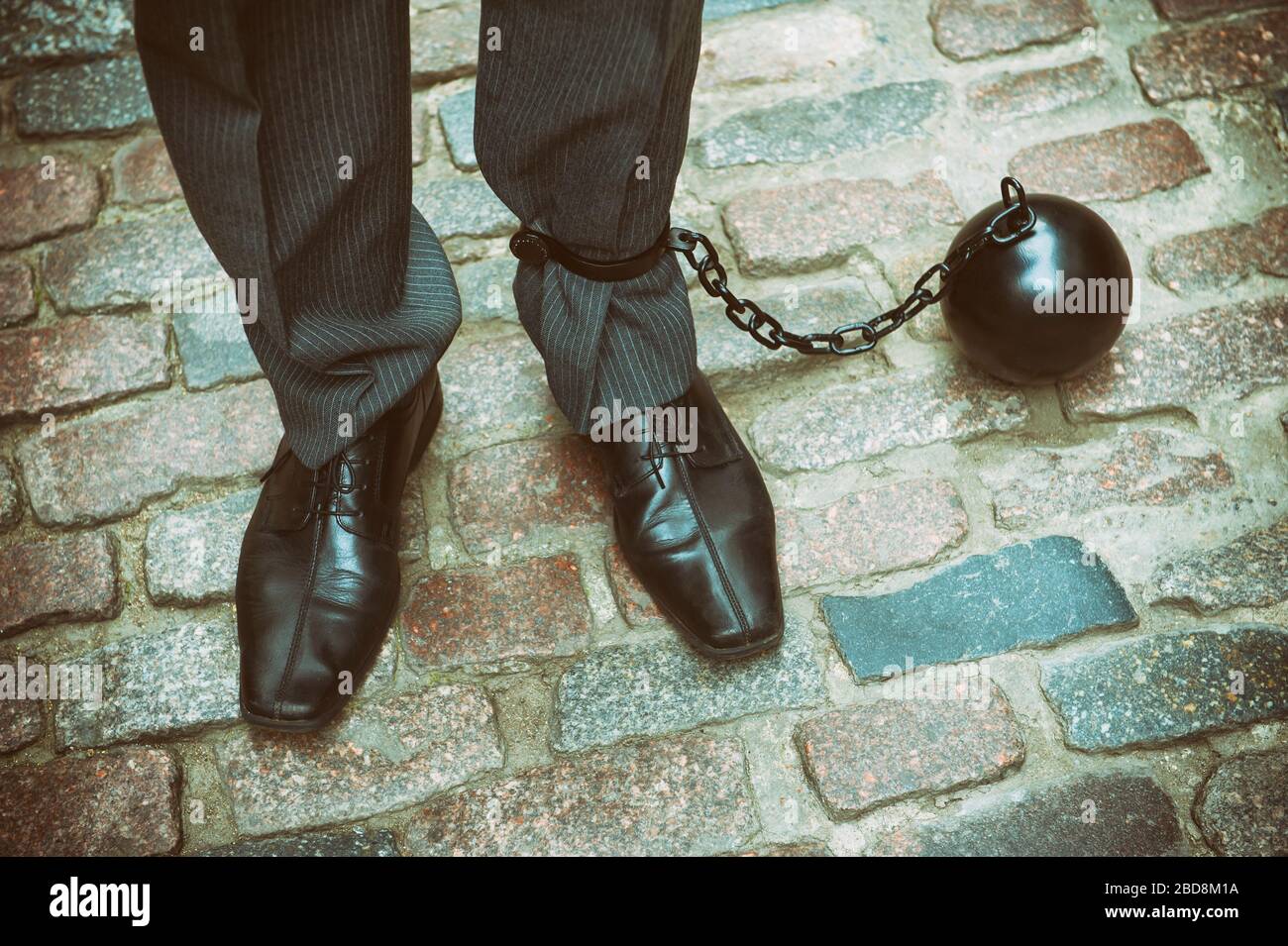 Unerkennbarer Geschäftsmann steht auf traditioneller Kopfsteinpflaster Straße mit großen schwarzen Eisenkugel an den Knöchel gekettet Stockfoto
