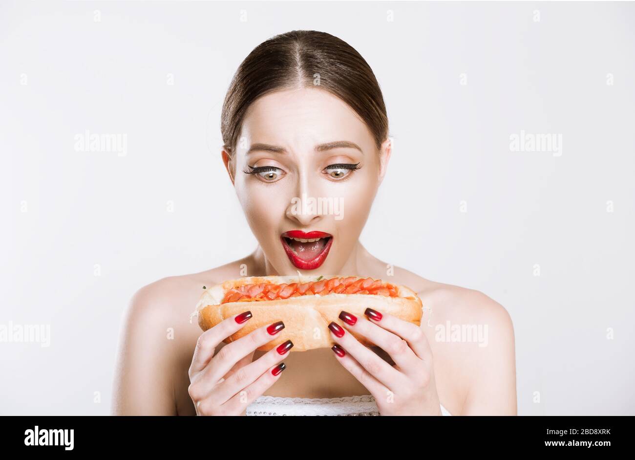 Schöne lustige Frau mit roten Lippen, die einen Burger hält, um zu beißen, essen isolierten weißen grauen Hintergrund. Ungesundes Essenskonzept Stockfoto