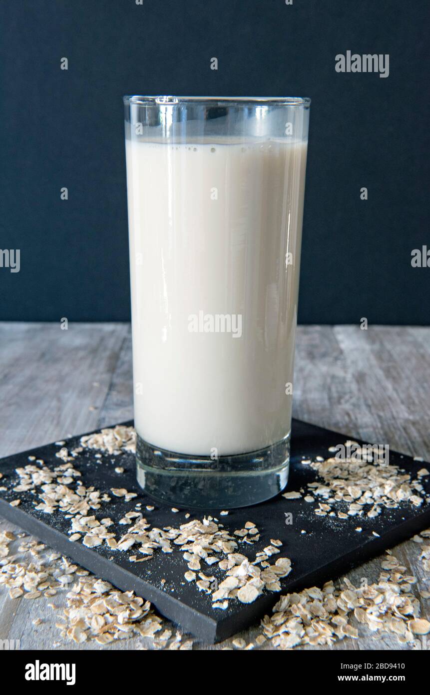 Vegane Hafermilch oder trinken in Glas mit Hafer, die auf schwarzen Fliesen mit schwarzem Hintergrund herumgestreut sind Stockfoto