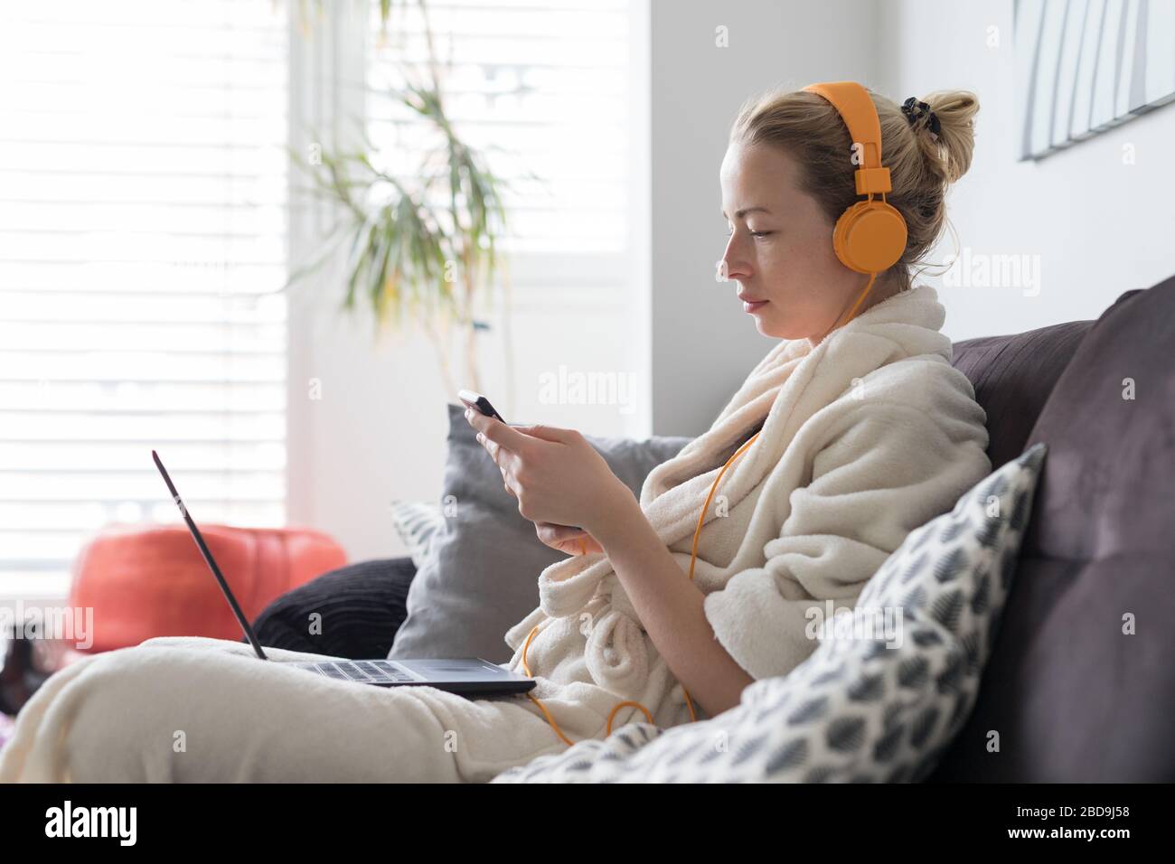 Soziale Distanzierung. Bleiben Sie zu Hause. Frau im bademantel ist bequem auf ihrem Sofa zu Hause und verwendet Social-Media-Apps auf dem Telefon für Videochats und Stying Stockfoto