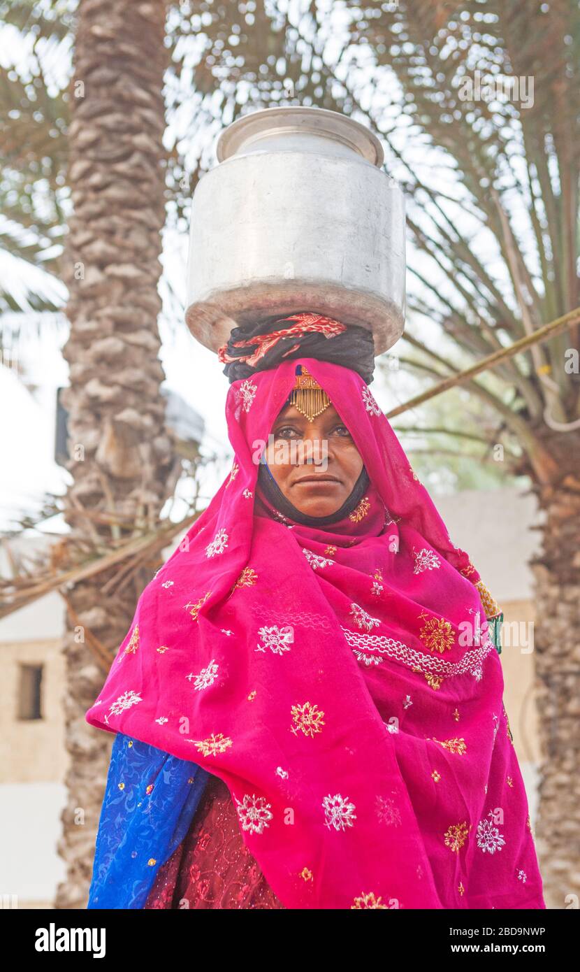 Eine omanische Frau im traditionellen Kleid, die eine Milchurne in einem Dorf im Sultanat Oman trägt. Stockfoto