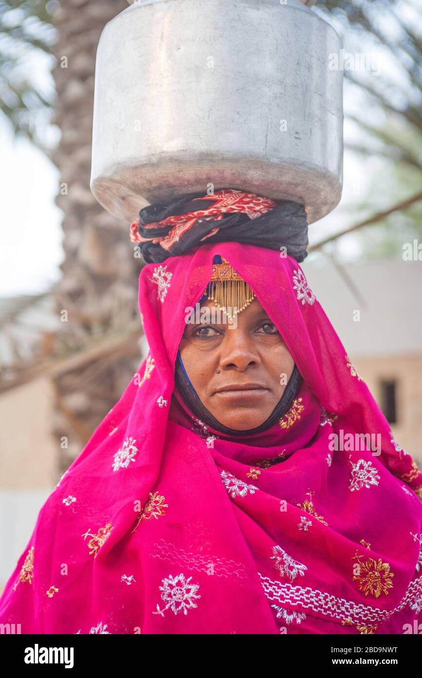 Eine omanische Frau im traditionellen Kleid, die eine Milchurne in einem Dorf im Sultanat Oman trägt. Stockfoto