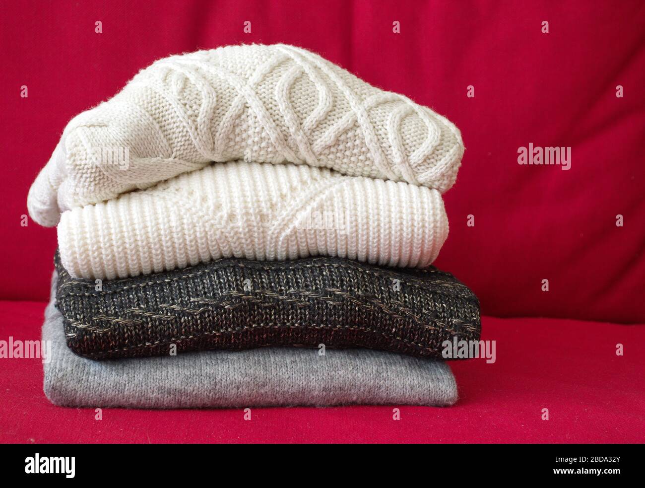 Nahaufnahme der warmen Pullover auf dem roten Sofa im Wohnzimmer Stockfoto