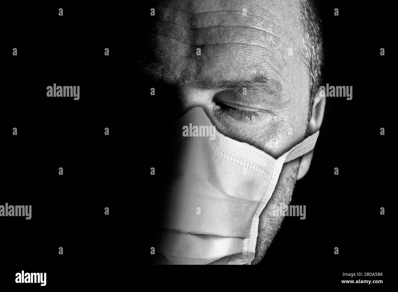 Dunkles und stimmungsvolles Porträt eines ernsthaft aussehenden männlichen Erwachsenen mit geschlossenen Augen, der sugikale Maks zum Schutz vor Coronavirus oder COVID-19 trägt Stockfoto