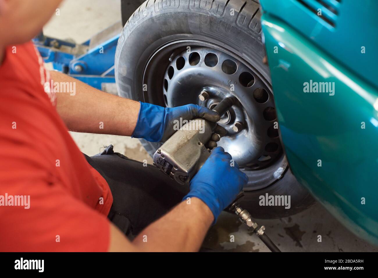 Nahaufnahme der männlichen Hände in blauen schmutzigen Handschuhen Installation Ansatzmuttern. Professioneller Mechaniker mit Schlagschrauber während der Arbeit in der Garage. Konzept des Autoservice. Stockfoto