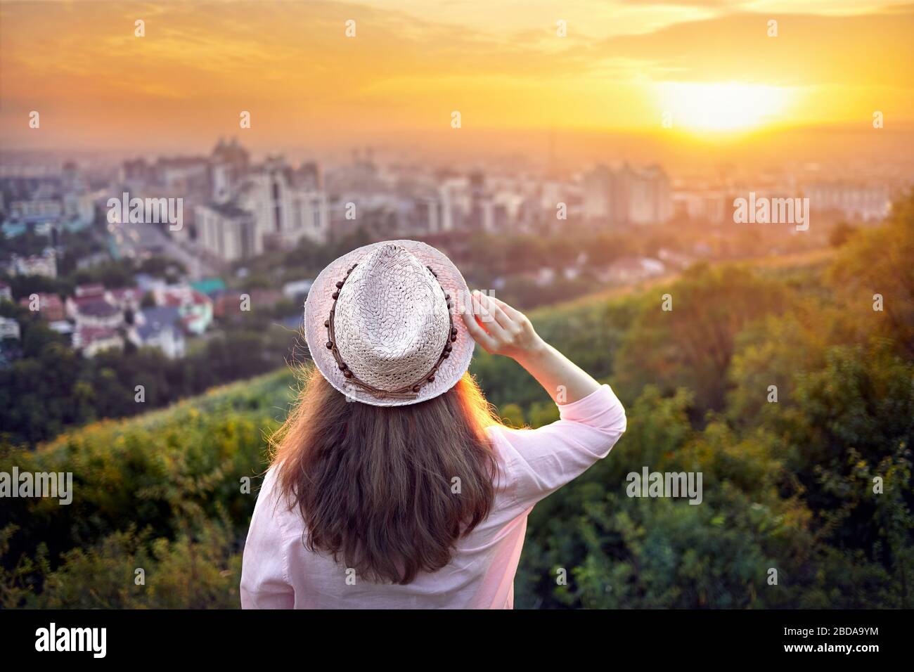 Frau mit Hut suchen bei Sonnenuntergang Blick auf die Stadt Hintergrund Stockfoto