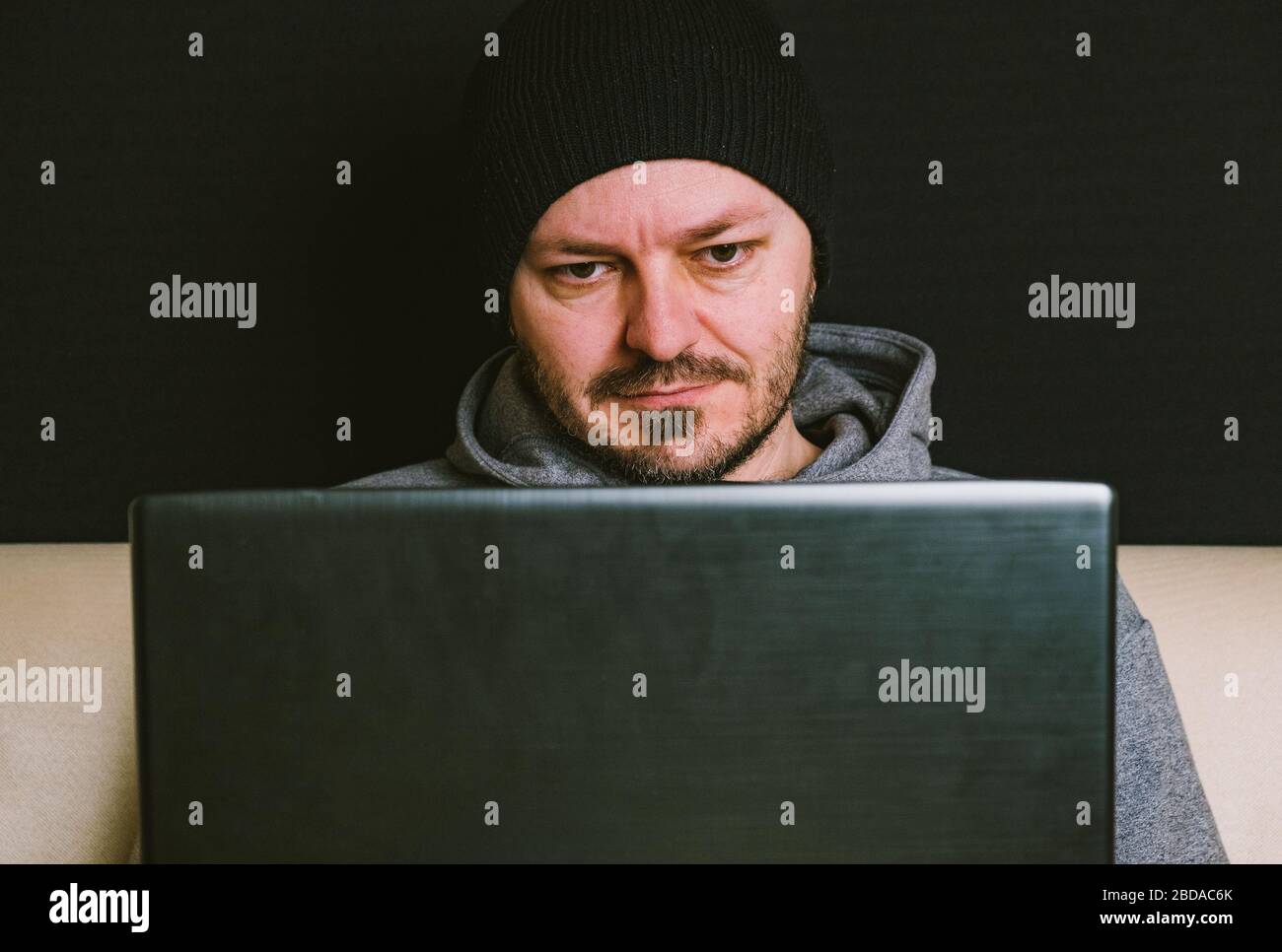 Mann trägt schwarze Mütze und Hoodie sitzt hinter dem Computer-Monitor in der Dunkelheit, Nahaufnahme, hacking Computer-System-Konzept Stockfoto