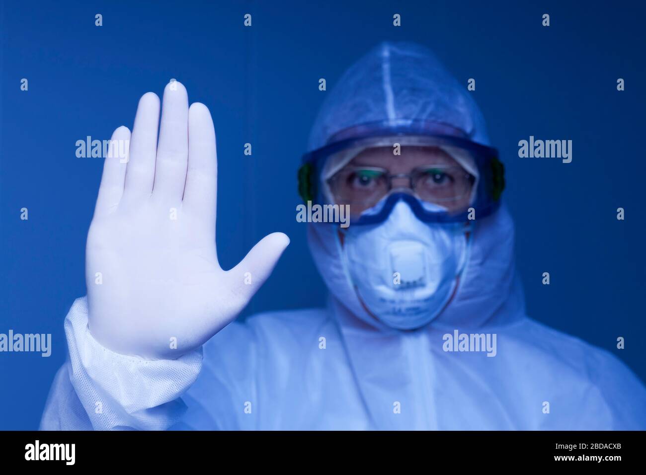 Arzt mit Schutzkleidung und ärztlicher Maske Gesturstopp mit der Hand - blaues Bild - Fokus auf der Hand Stockfoto