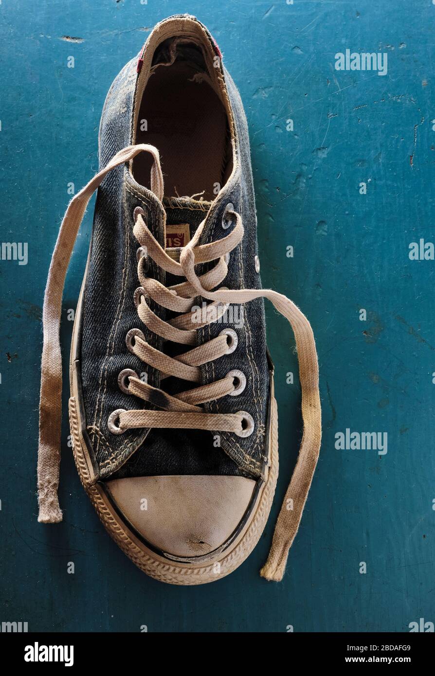 Hochauflösende Nahaufnahme eines einzigen alten und abgenutzten blauen Sneakers auf blauem Hintergrund mit Kopierfläche. Stockfoto