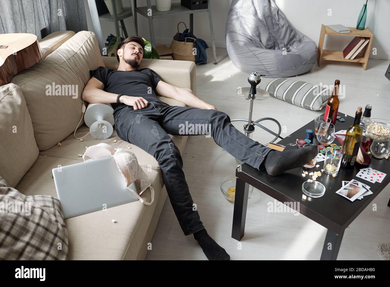 Müde betrunkene junge Mann schläft mit Lampe auf dem Sofa nach rauer Nachtparty in moderner Wohnung Stockfoto