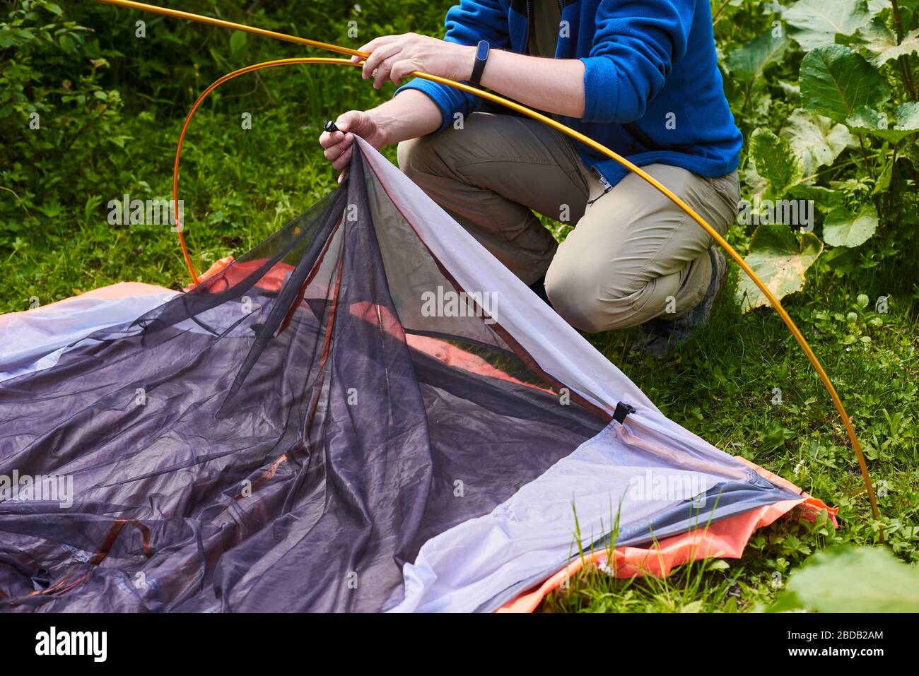 Touristen stellen ein Zelt auf einem Campingplatz auf. Schritt für Schritt Anleitung, wie man ein Zelt aufzustellen. Mann, der ein oranges Zelt im Wald aufgreift Stockfoto