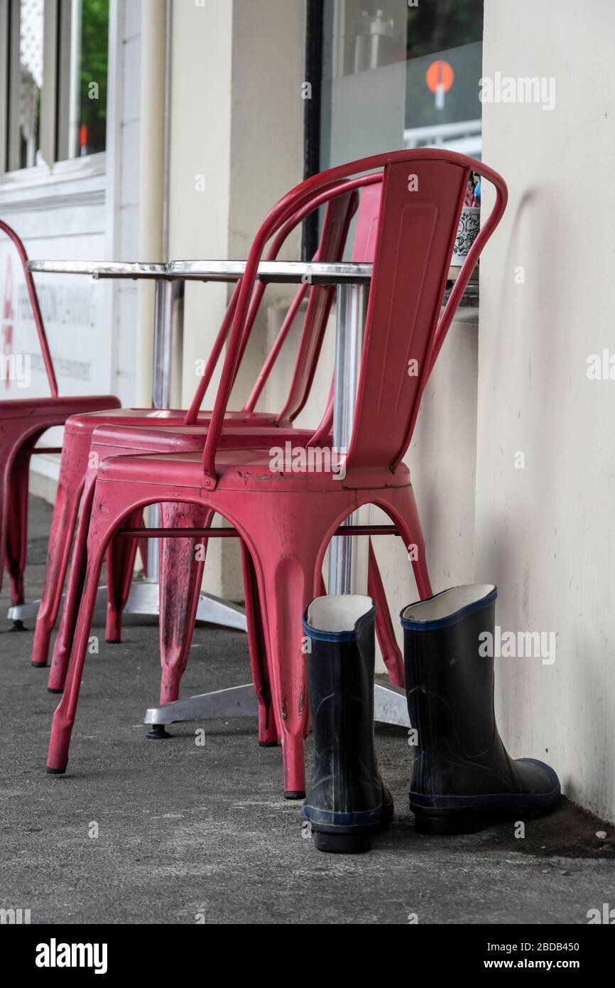 Gummistiefel neben einem rosa Stuhl vor einem Café in Martinborough, Wairarapa, Neuseeland Stockfoto