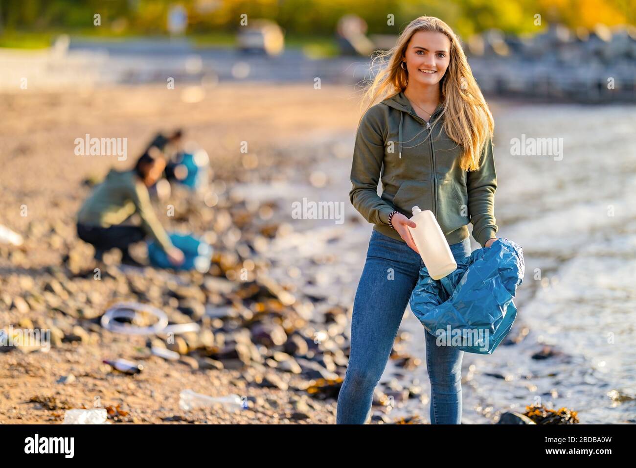 Wunderschöner junger Freiwilliger, der Flasche und Müllbeutel am Strand hält Stockfoto