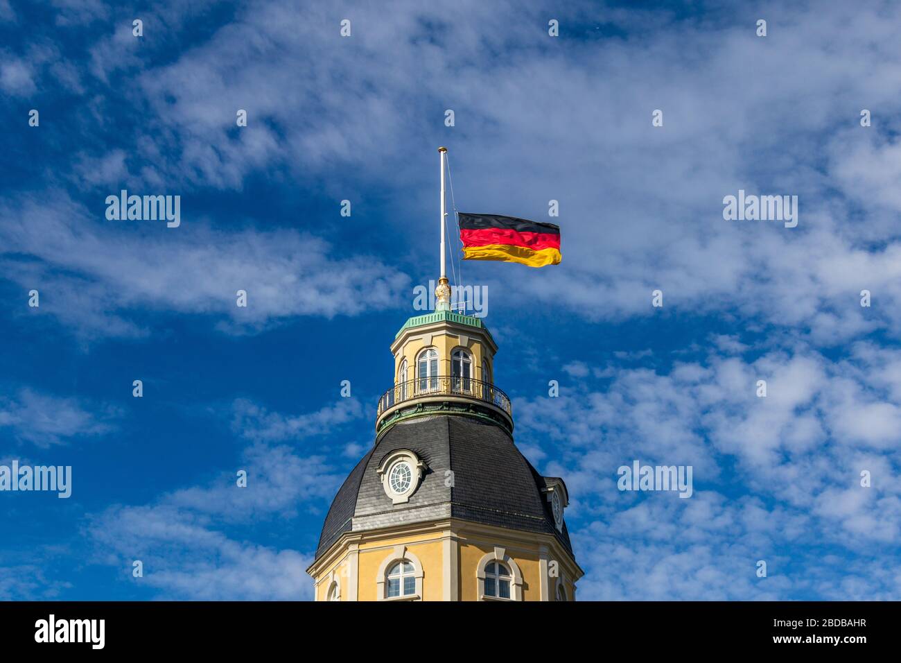 Deutsche Fahne am Halbmast, auf Halbmast, auf dem Turmdach von Schloss Karlsruhe, blauer Himmel dahinter. In Baden-Württemberg Stockfoto