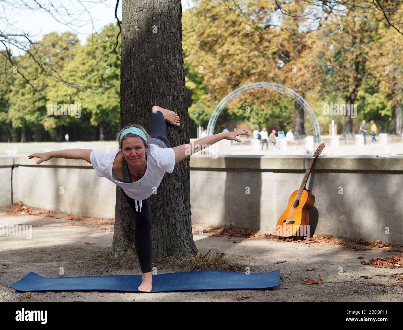 Mädchen, die eine Yoga-Pose draußen in einem Park Säugling eines Baumes mit einer Gitarre neben einer Wand gelehnt. Stockfoto