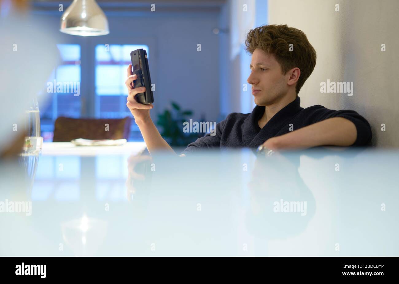 Porträt eines jungen gutaussehenden Mannes, der in seiner Wohnung sitzt und ein Handy in der Hand hält Stockfoto