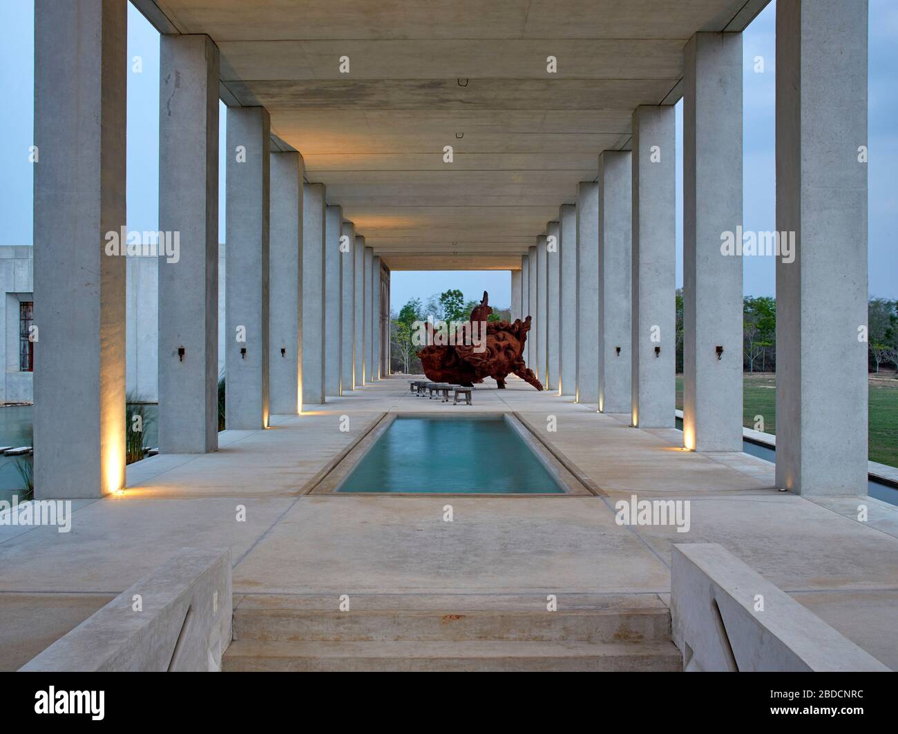 Blick über die Kolonnade mit Poolhalle im Freien und großer Skulptur darüber hinaus. Plantel Matilde, Yucatan, Mexiko. Architekt: Javier Marín und Arcadio Marín Stockfoto