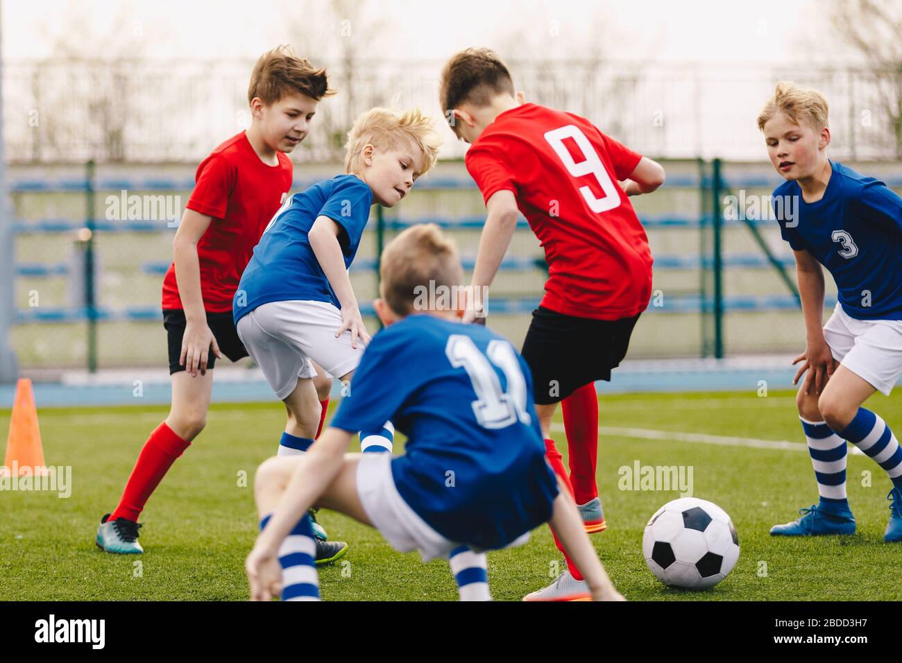 Schuljungen spielen Fußballspiel. Junge Spieler treten auf dem Sportplatz auf dem Fußballball an. Glückliche Kinder treten auf einem Feld an Stockfoto