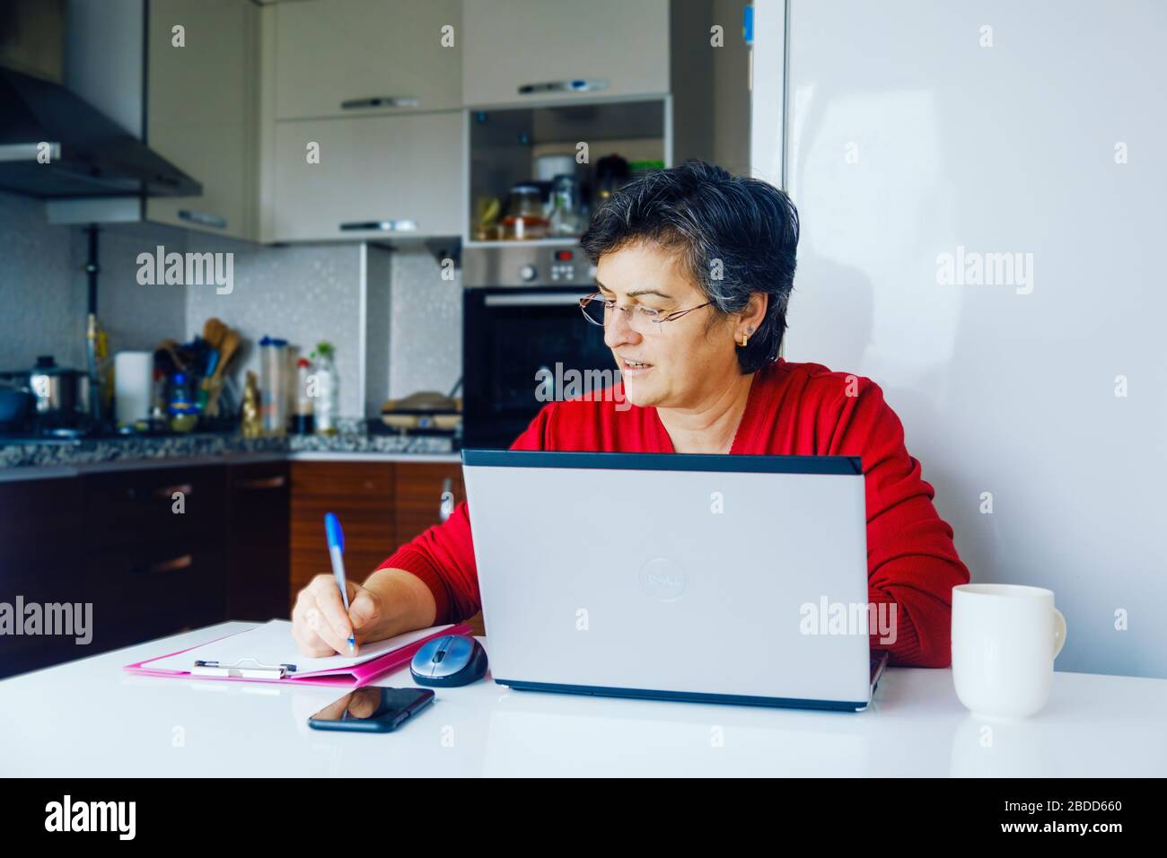 Erfolgreiche Geschäftsfrau mittleren Alters arbeitet an Quarantänetagen zu Hause in ihrer Küche. Stockfoto