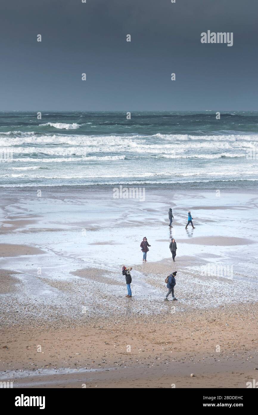 Menschen, die einen zügigen Spaziergang bei starken windigen Wetterbedingungen am Fistral Beach in Newquay in Cornwall genießen. Stockfoto
