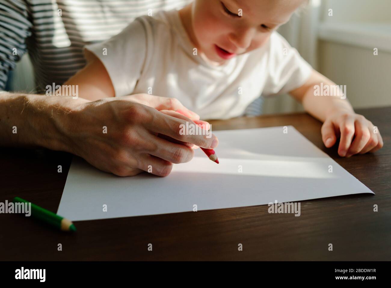 Vater, der dem Kind beigebracht hat, mit den Händen zu schreiben oder zu zeichnen. Roter Bleistift und Papier auf Holztisch. Homeschooling Stockfoto