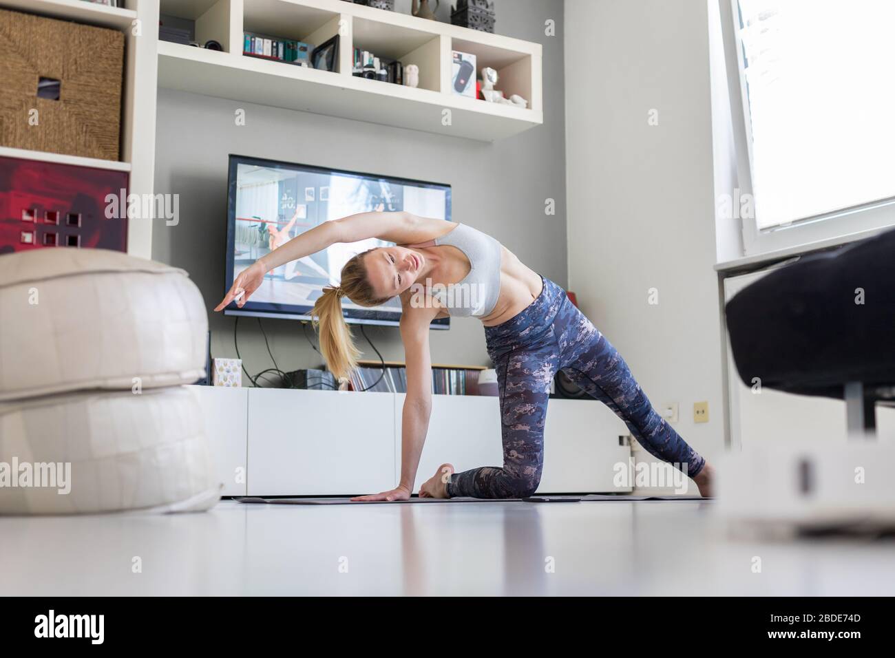 Attraktive sportliche Frau, die zu Hause arbeitet und Pilates vor dem Fernseher in ihrem Wohnzimmer Sport macht. Soziale Distanzierung. Bleiben Sie gesund und Stockfoto