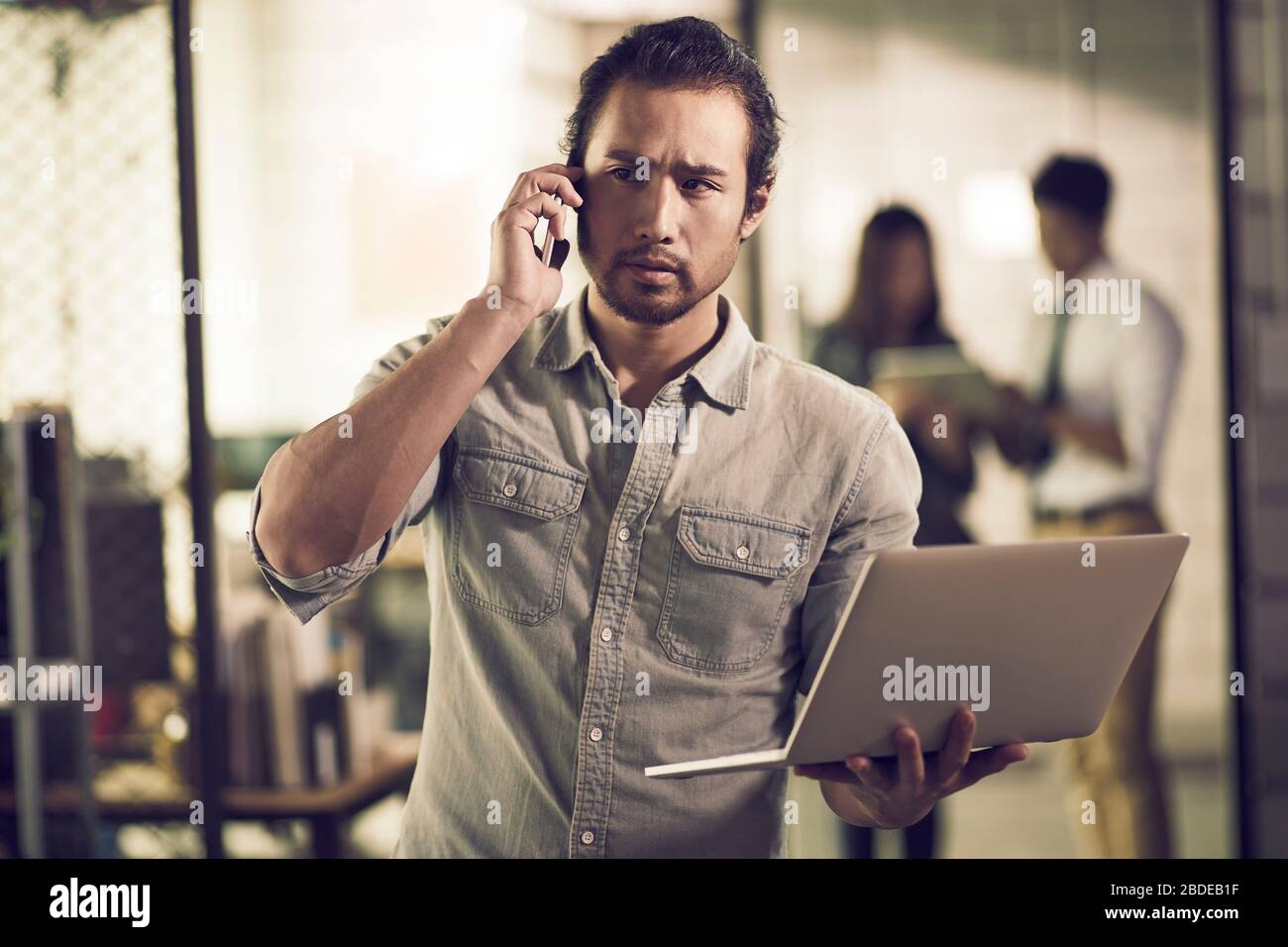 Unternehmer in Asien, der einen Laptop mit Telefon im Büro telefoniert Stockfoto