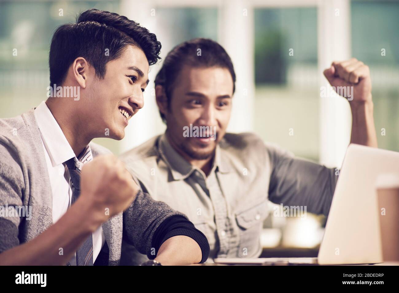 Zwei junge asiatische Kollegen arbeiten mit einem Laptop im Büro zusammen Stockfoto